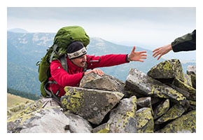 Backpacker reaching out his hand for help to climb over a rock